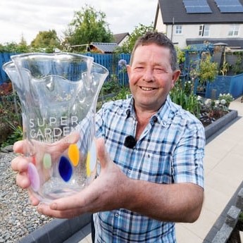 A headshot of Super Garden 2024 winner John Dooley holding his trophy in his winning garden - Back to the Future.